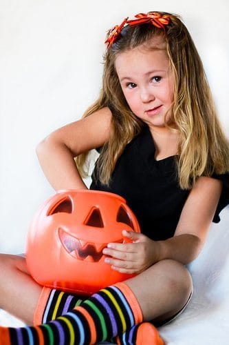 A young girl with her hand inside a jack o lantern full of Halloween candy