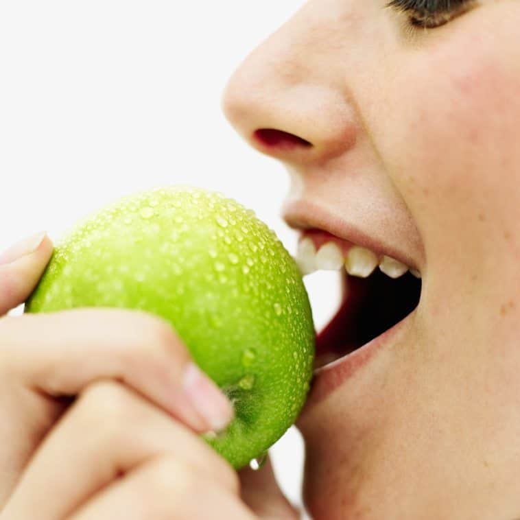 A woman biting into a green apple
